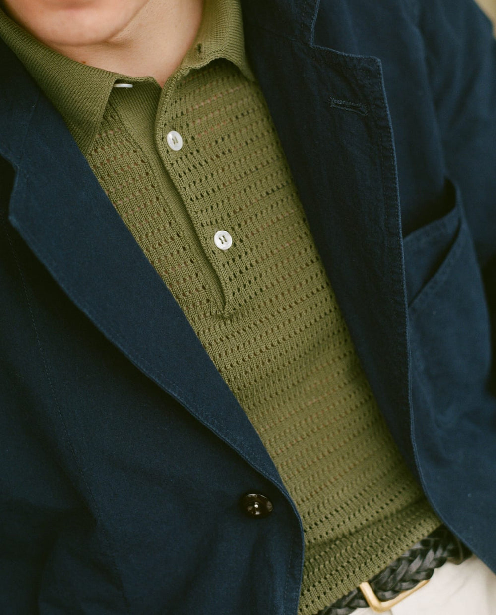 Close-up of a person wearing a green knitted polo shirt with a navy blazer.